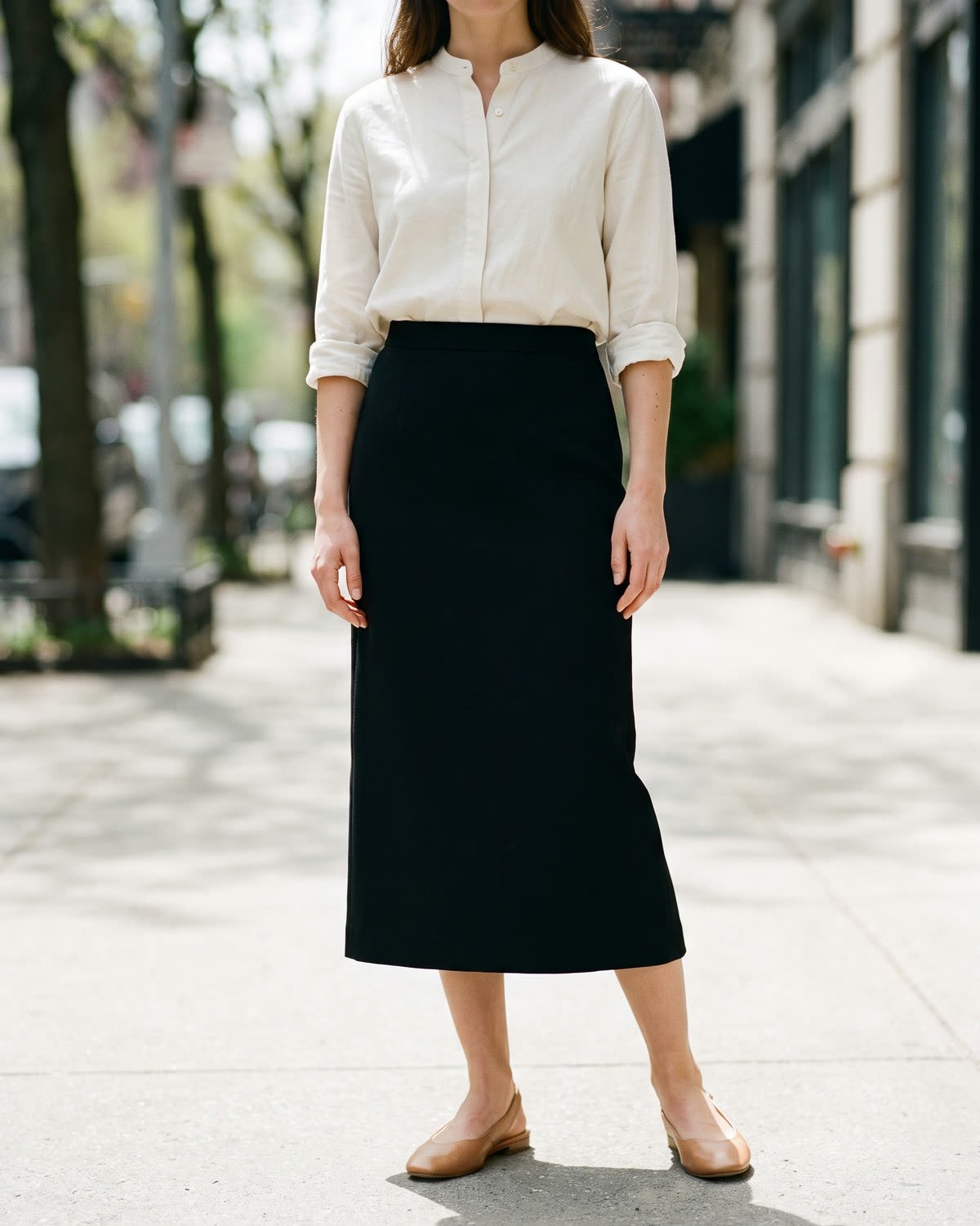 Chemise Sentier&nbsp;: chemise sans col en coton et lin écru, manches retroussées, rentrée dans une jupe midi noire.