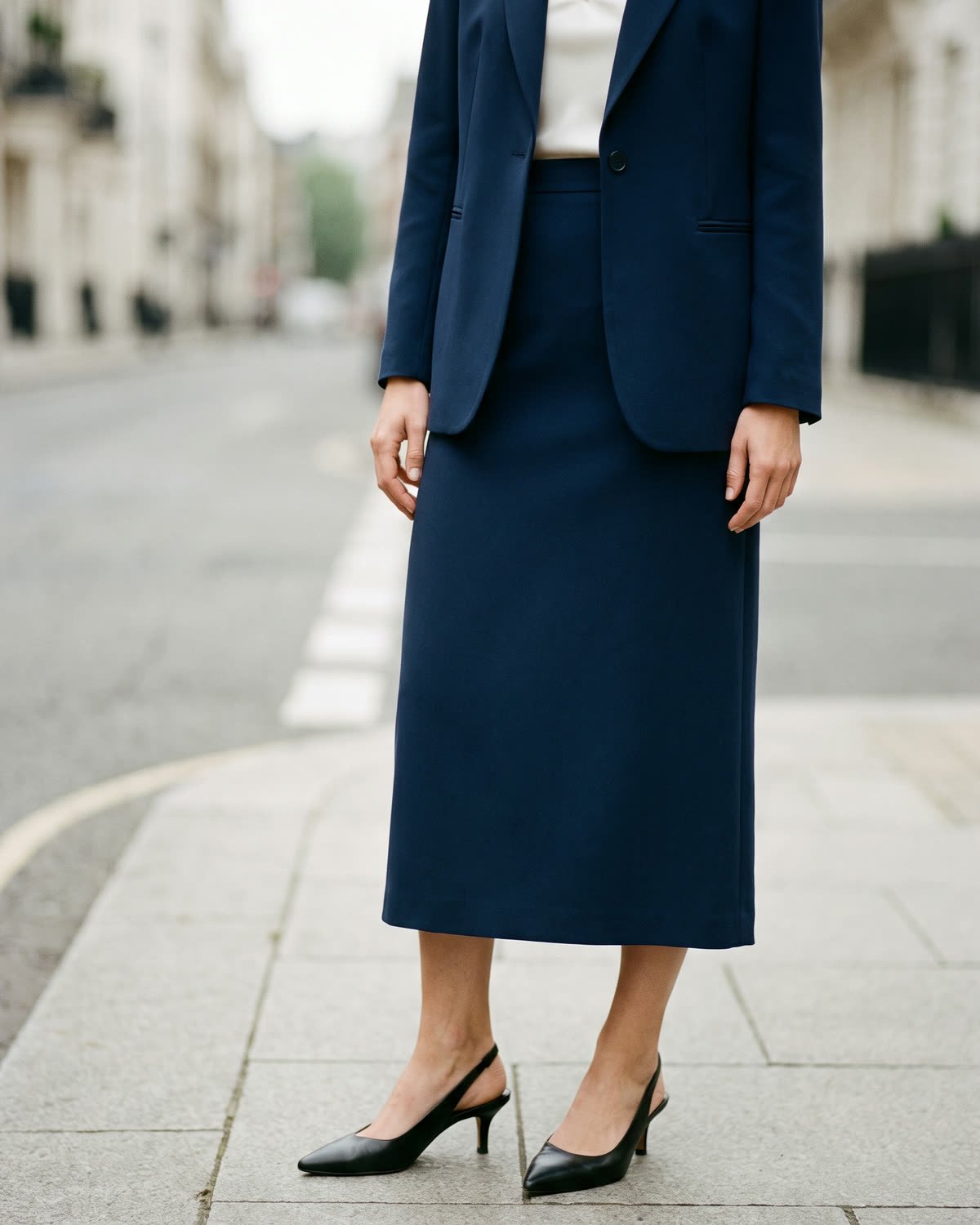 Veste Odéon&nbsp;: veste droite en crêpe de laine et soie bleu encre, fermée d'un bouton sur un haut ivoire.